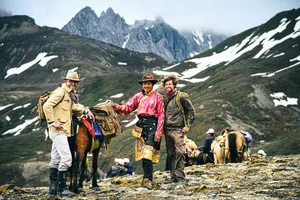 Backpackers meeting a mule caravan on a snowy, rocky mountain trail in Shangri-La’s high-altitude valleys