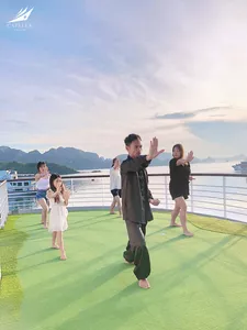 Barefoot stretching on the cruise deck yoga mat with calm sea and distant karsts behind on a Lyra Cruise Collection cruise in Halong Bay