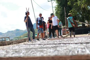 Group standing on a gravel path by the sea with greenery and mountains behind, looking out during a Labuan Bajo Komodo day trip