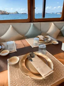Breakfast table set on a phinisi in Labuan Bajo, with plates, cutlery and patterned placemats by large sea windows
