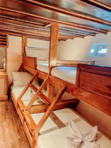 Twin guest cabin with wooden bunks and neatly folded towels on a deluxe phinisi, ready for a Komodo cruise from Labuan Bajo