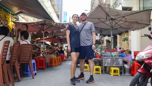 在胡志明市热闹的街市小巷里,两位旅行者撑着伞站着,参加 Jackfruit Adventure 的单车一日行程