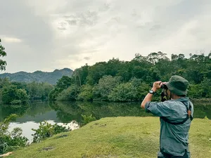 Nature lover photographing over a calm lake bordered by green hills and forest in Langkawi during a guided birdwatching stop
