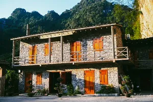 Rustic two-storey stone homestay with orange doors and a balcony in lush green hills, part of the borderland adventure