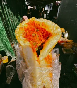 Stuffed golden flatbread sprinkled with red chilli spices held over wrapping at a lively Lijiang night market snack stall