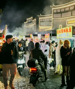 Bustling Lijiang night market crowd walks past neon-lit stalls and scooters, setting the scene for a local food hunt