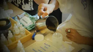 A cup pouring fragrance concentrate into a coco-soy candle jar on a Singapore worktable during a candle workshop