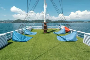 Private 3D2N Komodo cruise on a sleek white phinisi: green sun deck with blue lounging cushions and sail rigging in Labuan Bajo