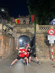 Travellers posing in a narrow illuminated laneway beneath an old stone arch during a Hanoi night food experience