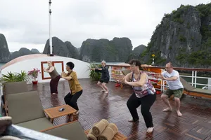 旅客们在吉婆岛精品游船的甲板上一起热身,身后是石灰岩峭壁和海上的薄雾