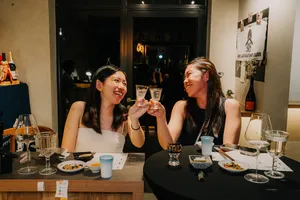 Guests toast at a rare sake tasting dinner in Singapore, smiling across a table of small dishes and shared glasses