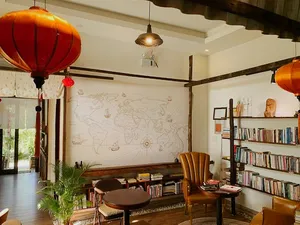 Area lounge di Chan Dat Living Room di Hoi An dengan kursi, rak buku, dinding peta dunia, dan lampion oranye gantung