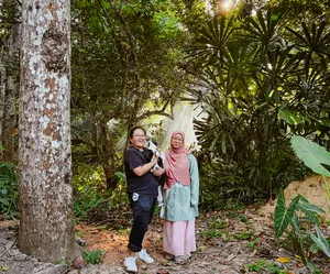 Two travellers standing in a shaded garden at Kebun Lidstari in Langkawi, surrounded by palms and dense tropical greenery