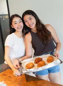 Two women smiling while sharing trays of baked shio pan buns after making flavoured butter during hands-on workshops in Singapore