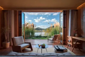 Lounge terbuka di eco retreat Linden Centre di Shaxi, Dali, dengan pintu kaca yang menghadap ke danau berpagar alang-alang