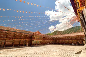 Prayer flags strung over a traditional Tibetan courtyard, with ornate wooden corridors and blue sky at Shangri-La