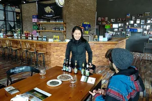 Smiling host pours while visitors sit at a wooden table with Tibetan beer bottles in a cosy brewery bar in Shangri-La