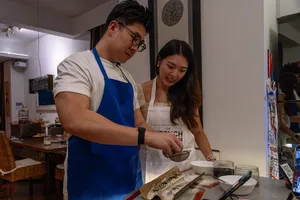 Host-led kitchen session: two people preparing food on a counter in a cosy Singapore loft, private dining Singapore
