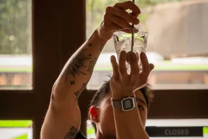 Para tamu saling mengangkat gelas koktail saat sesi cicip minuman racikan di bar intim di Singapura, ditemani cahaya hangat dan minuman dingin berisi es.