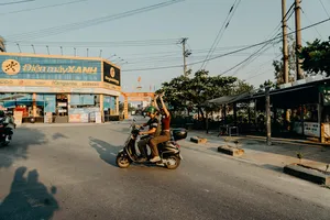 Dua pengendara Vespa mengangkat tangan saat melaju melewati deretan toko di Hoi An dalam perjalanan seru menyusuri jalan belakang bersama pemandu