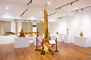 Museum-style gallery with a tall carved agarwood specimen on a pedestal among other wood displays in Hanoi