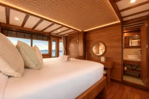 Komodo Island phinisi cabin bedroom with a large double bed, warm wooden walls and a round mirror, Travass Life 3D2N stay