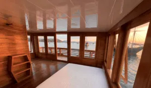 Wooden phinisi lounge with windowed walls and a view over the Komodo waters on a shared 3D2N cruise from Labuan Bajo