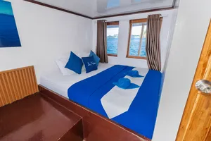 La Famille cabin with neat blue bedding, window curtains and sea water visible beyond, Komodo boat trip, Labuan Bajo