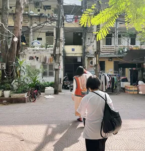 Walkers in matching vests on a quiet laneway in Hanoi, passing potted plants, laundry lines and old apartment blocks.