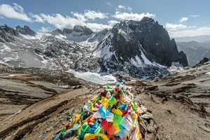 Colourful prayer flags on a rocky pass overlooking snowy peaks in Shangri-La, surrounded by rugged hiking terrain