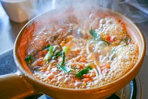 Steaming Yunnan hotpot-style soup with noodles and herbs simmering in a clay bowl during a Lijiang cooking experience