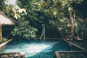 Person strolling by a lush infinity pool under thatched umbrellas in a tropical garden at a Bali retreat