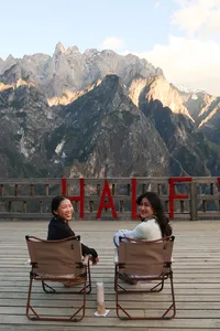 Travellers seated on folding chairs on a viewing deck with towering peaks of Tiger Leaping Gorge near Lijiang