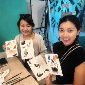 Art For Good art therapy in Singapore: two women seated at a craft table showing pet-themed cards during workshops in Singapore
