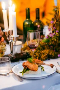 Candlelit 3-course dinner plate with sliced grilled chicken and herbs, with wine glasses on a table during Ferme Liotard’s trek