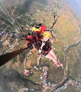Tandem paragliding over stepped hillside rice terraces with two orange-helmeted riders holding the lines in mid-flight in Sapa