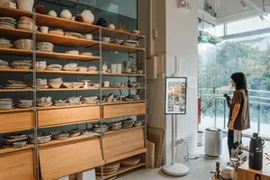 Rows of handmade ceramic plates on tall shelving in Ina Atelier’s Singapore studio, with a person standing by the window