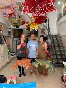 Three visitors posing with handmade red and green paper kite lanterns in a Saigon craft shop led by Viet Awesome Tours