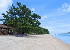 Pantai yang tenang di Kepulauan Gili, Lombok, dengan pondok beratap rumbia, air yang tenang, dan sebuah bot kecil yang sedia untuk sesi snorkel peribadi