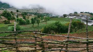 Misty countryside near Lijiang with a fenced foreground and a rural village of white houses as clouds roll through the valley