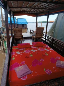 Outdoor boat deck with red bedding and two wicker chairs, set for relaxing between sightings on a 3D2N Sister Tour cruise, Tanjung Puting