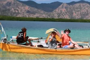 Friends seated on a small wooden boat on bright turquoise water with mountains behind them near Labuan Bajo