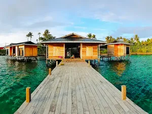 Timber overwater walkway leading to wooden chalets at Luma Selakan sea lodge in Semporna, surrounded by clear green sea
