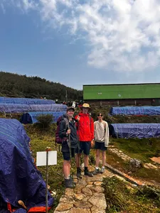 Trekkers standing by blue camping tarps near a green-roof shelter in Sapa during a Fansipan eco trek on the Hmong trail