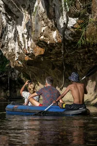 Family seated on an inflatable raft in dark lake water, drifting near rock walls at Khao Sok