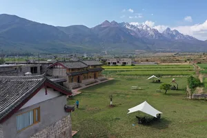 Lijiang coffee estate courtyard: traditional timber buildings, white tents on a green lawn, and misty mountains beyond