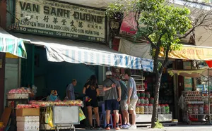 在胡志明市一家越南街头市场摊位前浏览商品的旅行团游客,周围摆满了罐装货品,头顶是遮阳篷