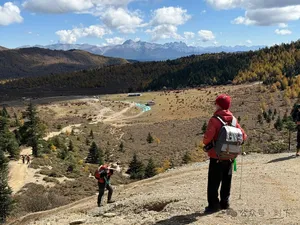 Backpacker looking over a valley from a ridge during the hidden alpine lake trek in Shangri-La, with group hikers below