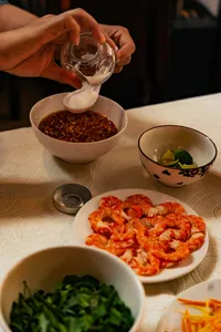 会安 Jolie 烹饪课：双手将香料酱汁倒入碗中，旁边摆着装盘好的虾和新鲜香草，呈现越南家常料理