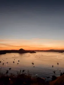 Warm sunset over a calm bay with anchored boats, seen from the shoreline during a Komodo cruise departing Labuan Bajo